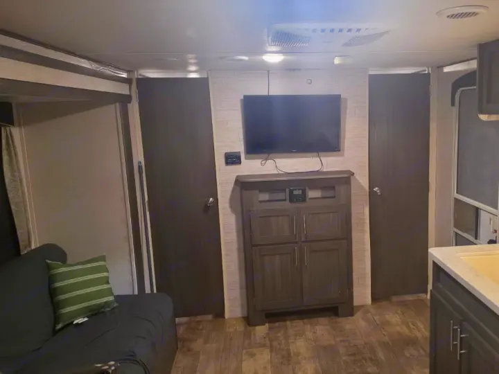 This rv rental features a cozy living space with a dark sofa, TV, cabinet storage, and warm wood-look flooring.. Shasta Shasta 2020