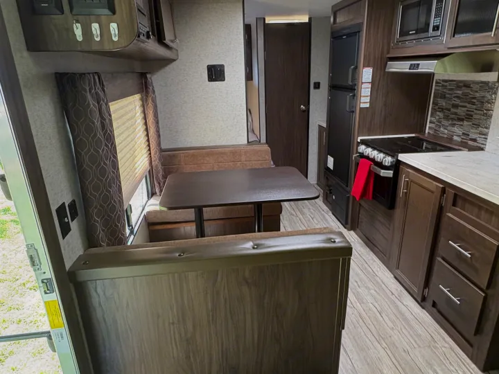 Inside an rv rental: a well-appointed dinette area with table and upholstered seating next to a functional kitchen with appliances.. Forest River Cherokee Grey Wolf 2018