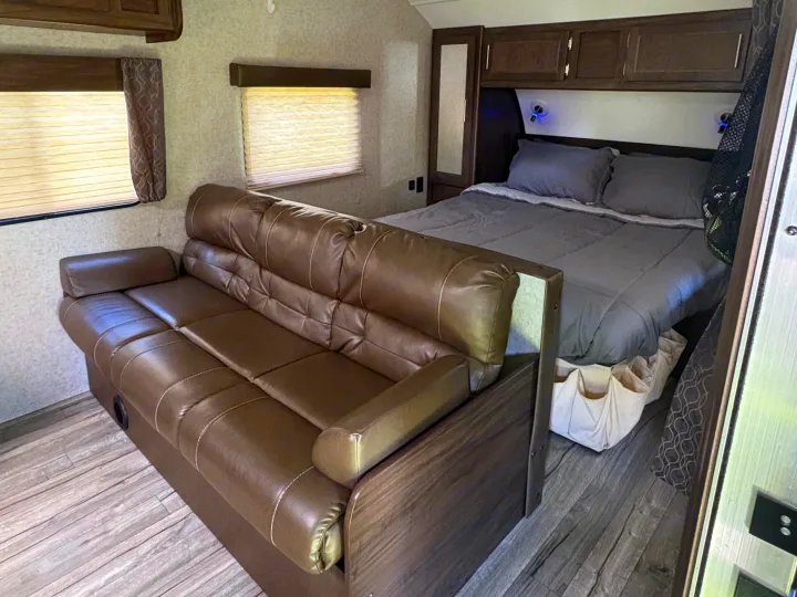 Inside this RV rental: a brown faux leather sofa and a bed with gray bedding, flanked by windows and cabinets.. Forest River Cherokee Grey Wolf 2018
