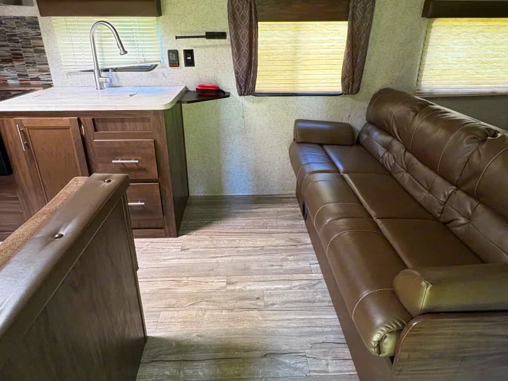 Modern RV rental interior featuring a full kitchen with sink, comfy leather sofa, and dinette seating.. Forest River Cherokee Grey Wolf 2018
