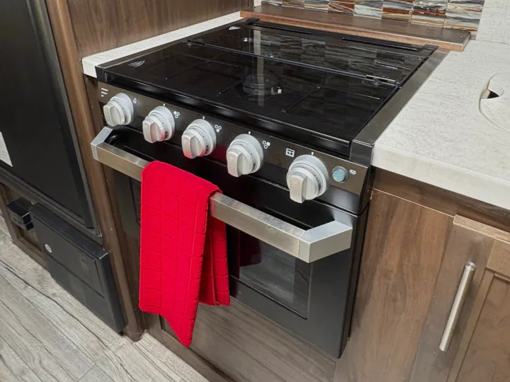 RV rental kitchen featuring a clean black stove, oven, and glass stovetop cover, with a bright red dish towel.. Forest River Cherokee Grey Wolf 2018