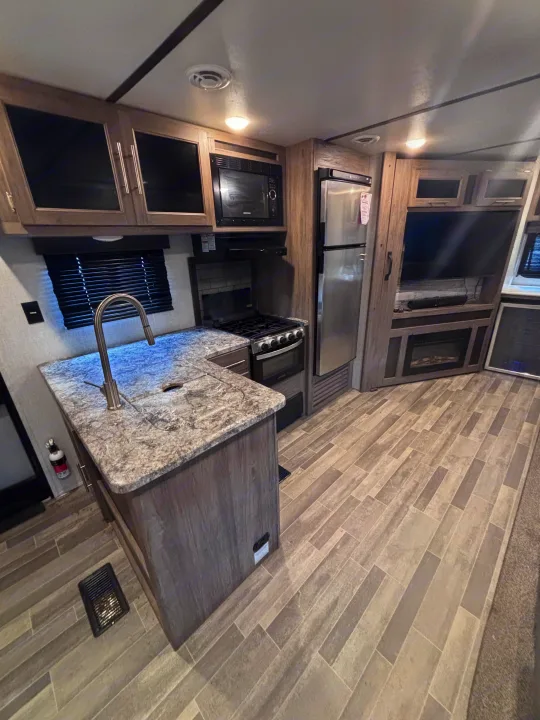 Modern RV rental interior featuring a full kitchen with stainless steel appliances, entertainment center, and an electric fireplace.. Crossroads RV Zinger 2021