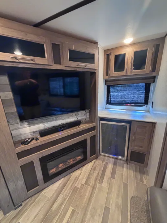 Interior of a modern RV rental featuring a large TV, electric fireplace, built-in mini-fridge, and overhead storage.. Crossroads RV Zinger 2021