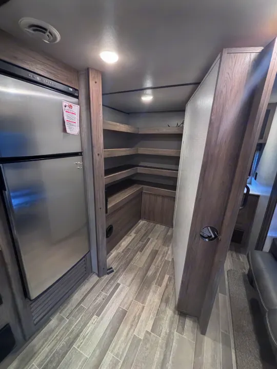 RV rental interior: kitchen with a large stainless steel refrigerator, open pantry shelves, and grey tiled flooring.. Crossroads RV Zinger 2021
