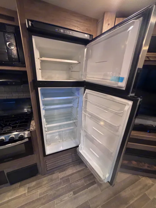 Empty RV rental kitchen with open refrigerator/freezer, microwave, and stovetop. Ready for your adventure!. Crossroads RV Zinger 2021