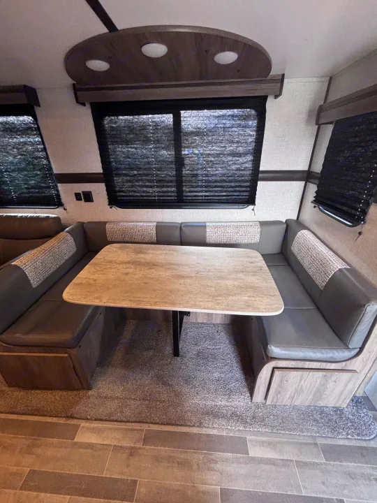 Cozy RV rental dinette with U-shaped booth seating, a light table, and privacy window blinds for a comfortable travel experience.. Crossroads RV Zinger 2021