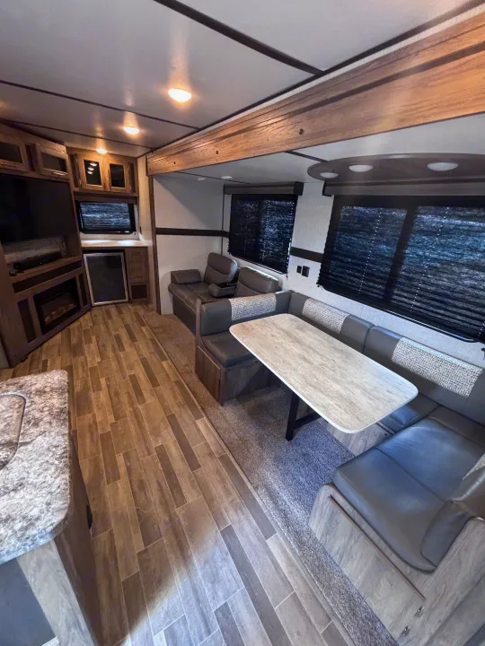 Inside a stylish RV rental: comfortable dining booth, lounge seating, TV/fireplace, and modern kitchen corner.. Crossroads RV Zinger 2021