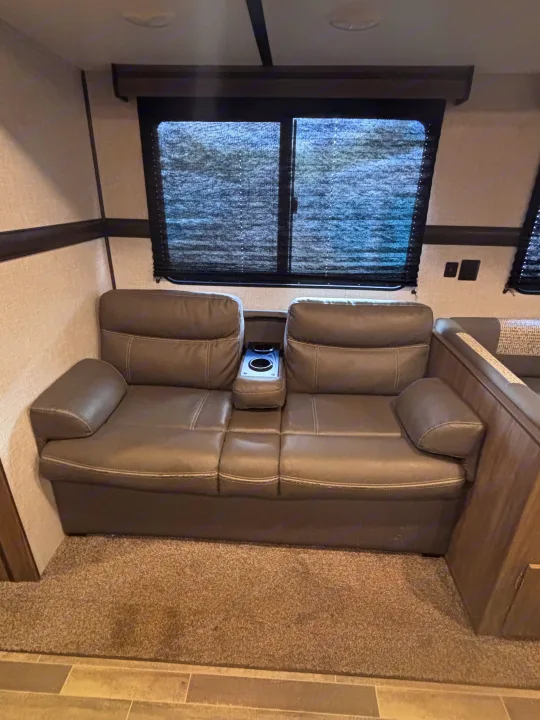 Inside an RV rental: a cozy, grey two-seat reclining sofa with integrated cup holders and a center console.. Crossroads RV Zinger 2021