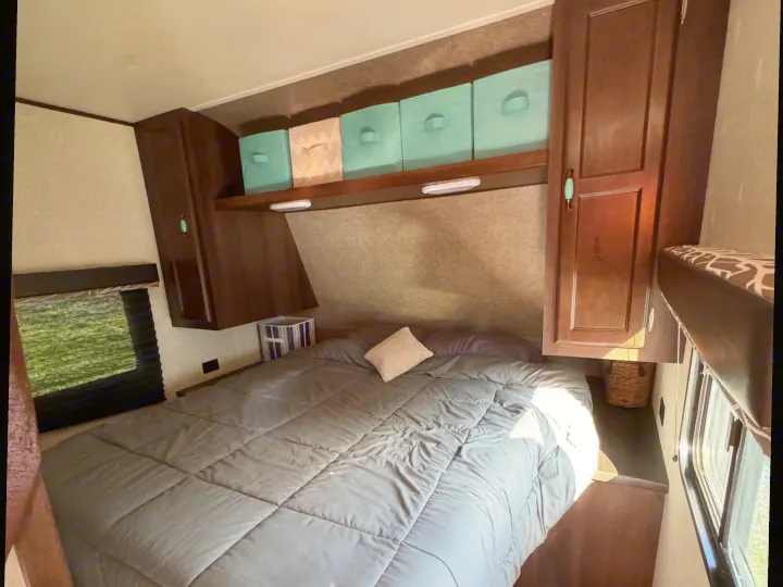 Cozy RV rental bedroom with a comfortable bed, built-in dark wood cabinets, and convenient overhead storage bins.. Jayco Jay Flight SLX Baja Edition 2018