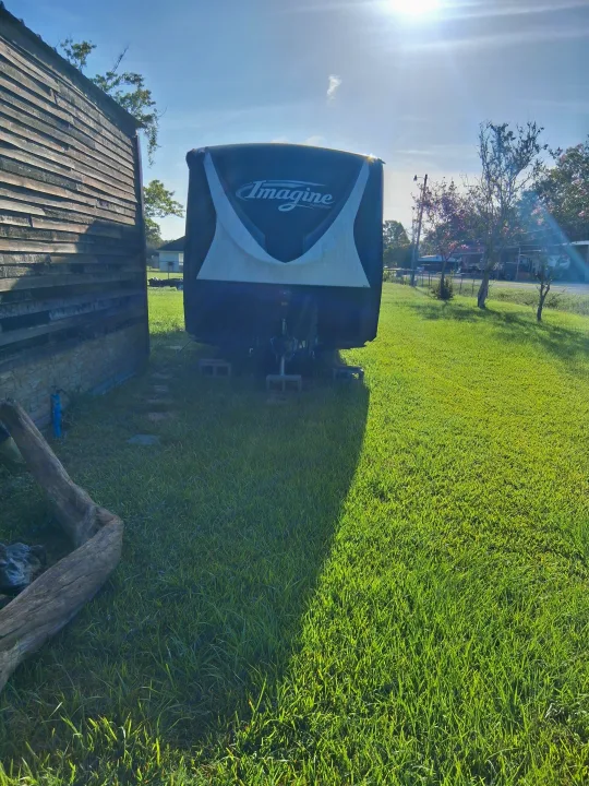Grand Design Imagine rv rental parked in a sunny, grassy yard beside a rustic wooden building.. Grand Design Imagine 2021