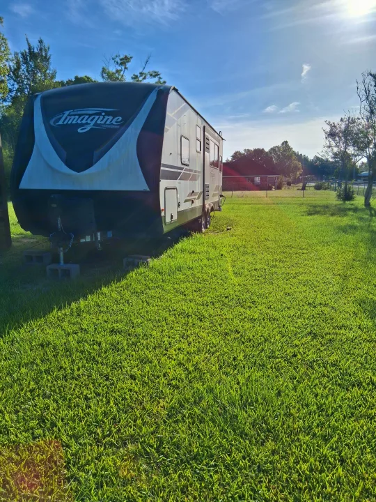 This Imagine travel trailer, set for an RV rental, rests on vibrant green grass under a bright blue sky, perfect for camping.. Grand Design Imagine 2021