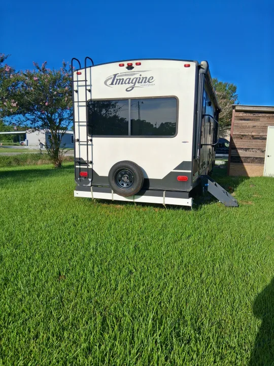 White Imagine Grand Design RV rental parked on grass. Rear view showing ladder, spare tire, and clear blue sky overhead.. Grand Design Imagine 2021