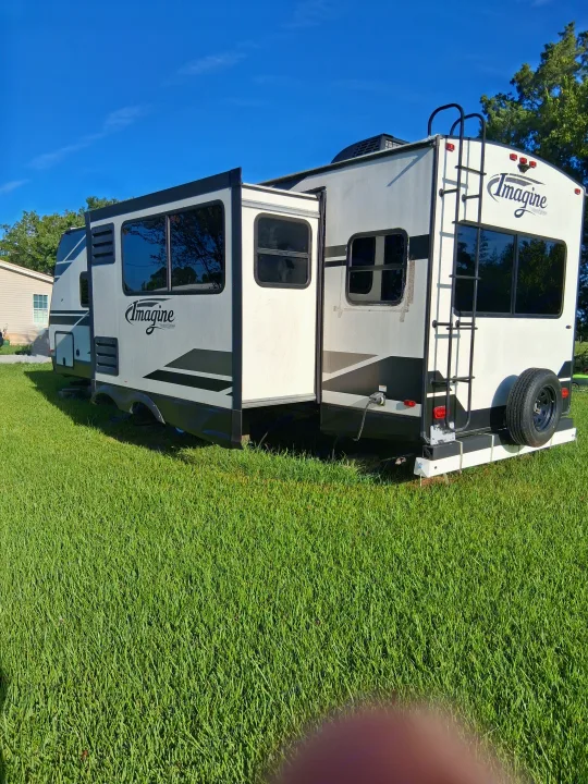 Spacious Imagine RV rental, a white travel trailer with slide-out extended, parked on green grass under a blue sky.. Grand Design Imagine 2021