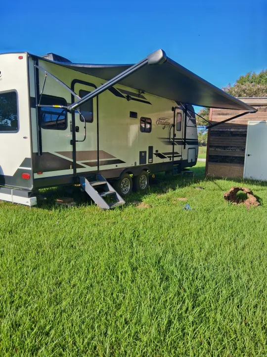 Imagine brand travel trailer, an RV rental, with awning out, parked on green grass under a clear blue sky.. Grand Design Imagine 2021