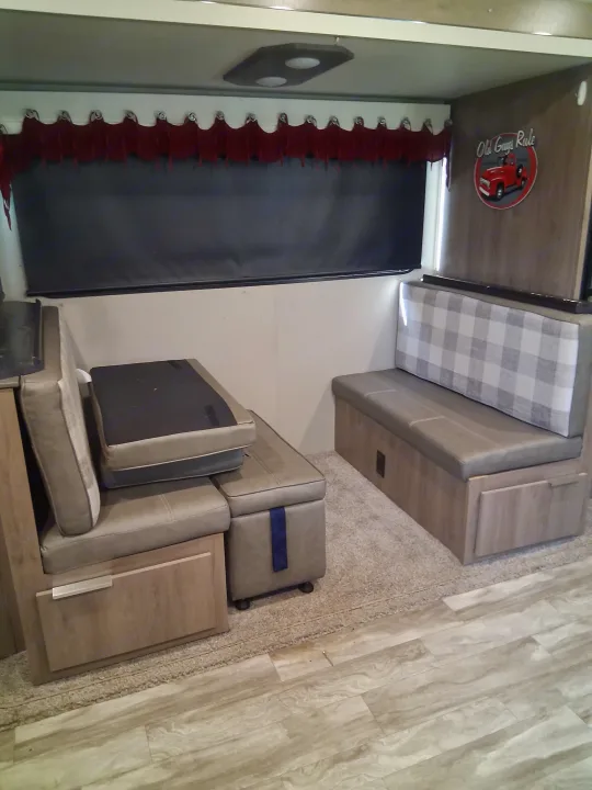 RV rental interior: cozy dinette with plaid backrest, storage under benches, versatile cushions, and a dark window shade.. Grand Design Imagine 2021
