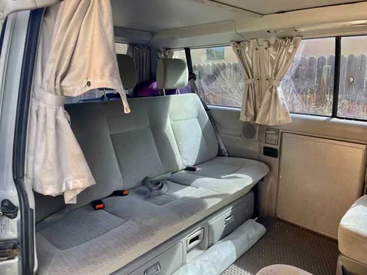 RV rental interior: light gray rear bench seat with storage below, and tied-back window curtains create a cozy camper experience.. Eurovan Camper Eurovan Camper Class B 2002