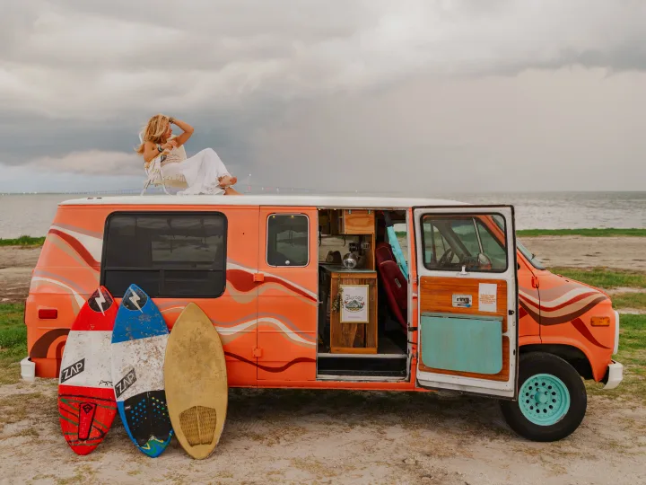 This rv rental sets the scene for adventure! A woman relaxes atop a retro van with surfboards, overlooking the ocean.. Chevrolet G20 Chevy Van 1990