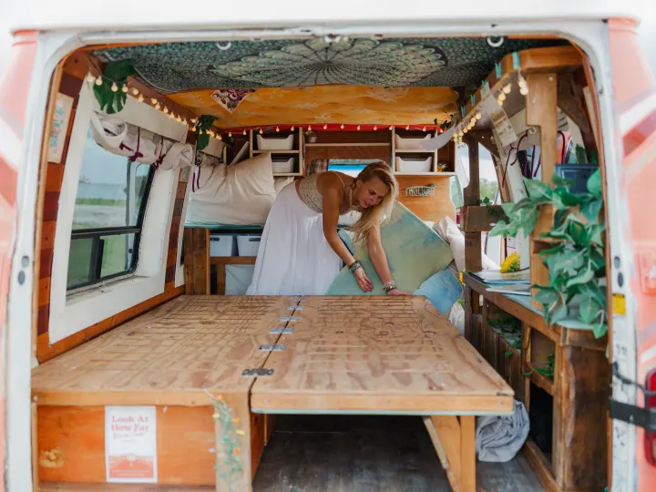 Woman arranges a cozy, bohemian camper van interior with wooden bed, perfect for an RV rental adventure.. Chevrolet G20 Chevy Van 1990