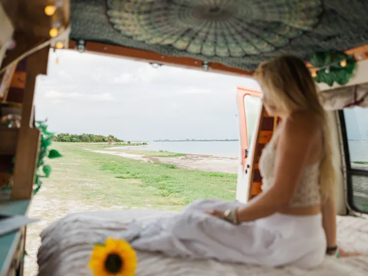 Enjoying the view from an RV rental: a woman sits looking out at a calm lake and green shore, with a sunflower nearby.. Chevrolet G20 Chevy Van 1990