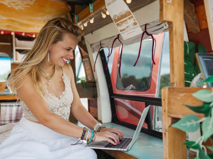 Smiling woman happily working on her laptop inside a cozy RV rental, enjoying remote work on the go.. Chevrolet G20 Chevy Van 1990