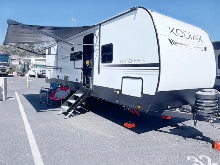 A white Kodiak Dutchmen RV rental with an extended awning and steps, parked for a sunny outdoor adventure.. Dutchmen Kodiak 2026
