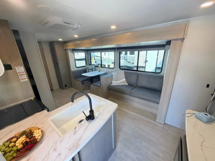 Bright RV rental interior featuring a modern kitchen with a large sink, dining booth, and a comfortable sofa by the windows.. Dutchmen Kodiak 2026