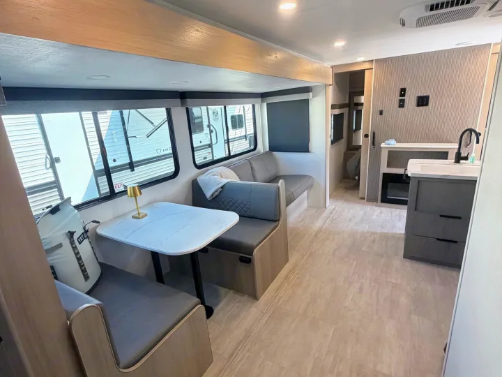 Modern rv rental interior: dinette, sofa, and kitchenette with sleek finishes. Light grey and wood tones throughout.. Dutchmen Kodiak 2026