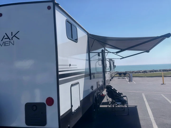Enjoying an RV rental by the ocean. White travel trailer with awning, chair, and scenic water view.. Dutchmen Kodiak 2026