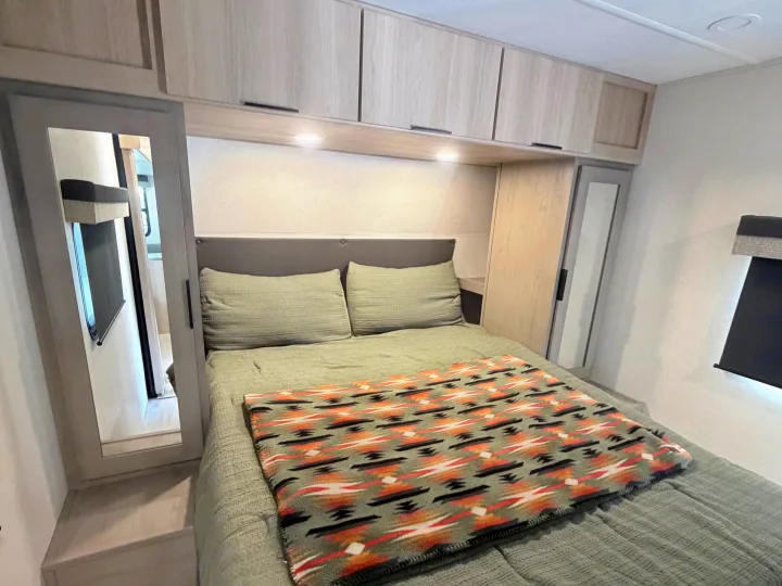 Cozy RV rental bedroom featuring a comfortable bed with a green comforter and Southwestern-patterned blanket, plus modern cabinets.. Dutchmen Kodiak 2026