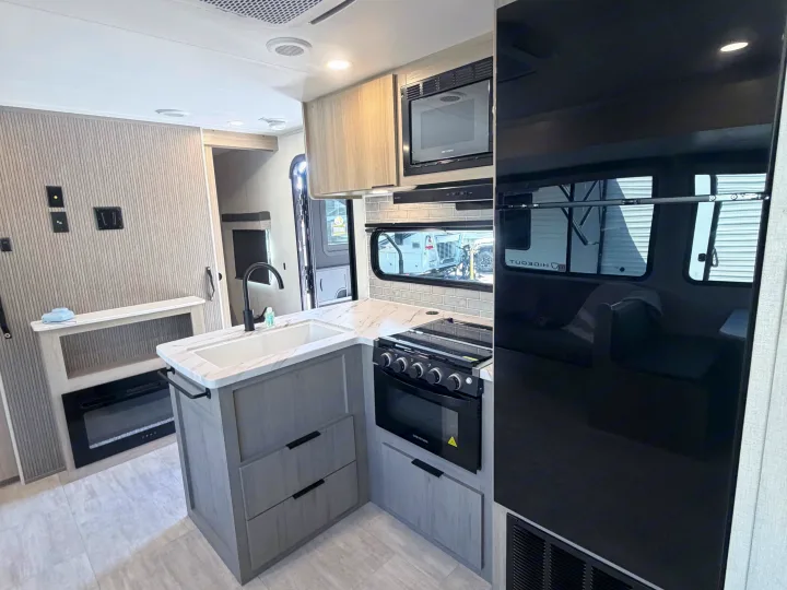 Modern RV rental interior: kitchen with sink, stove, microwave, fridge, and living area with electric fireplace. Perfect for travel comfort.. Dutchmen Kodiak 2026