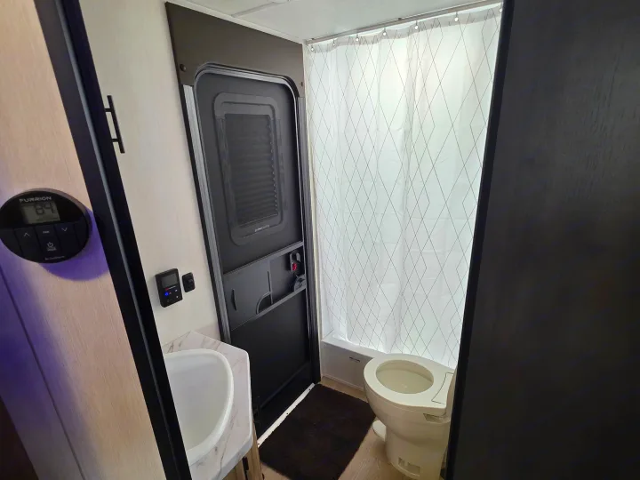 Compact rv rental bathroom with a toilet, patterned shower curtain, sink, and entry door, showing interior details.. Forest River Cherokee Grey Wolf 26KF 2026