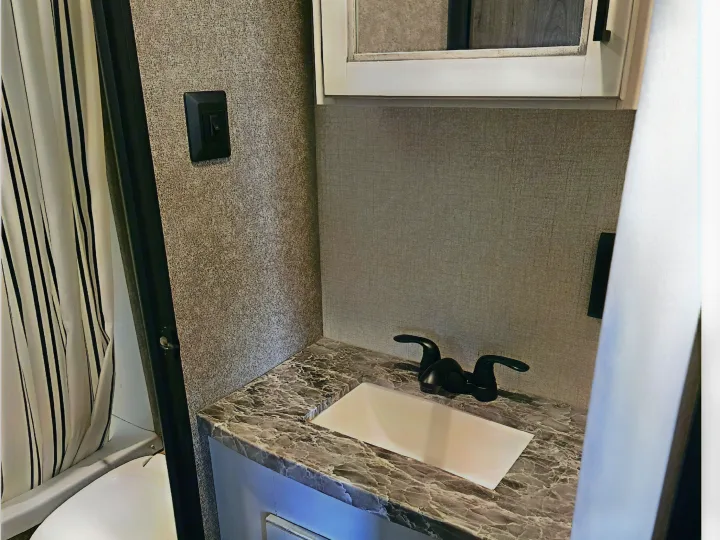 Explore this RV rental bathroom: featuring a striped shower curtain, compact vanity with marbled countertop, sink, and faucet.. Highland Ridge RV Open Range 2021