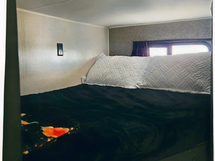 Cozy RV rental bedroom with a bed featuring a dark comforter, light quilted pillows, and a window.. Highland Ridge RV Open Range 2021