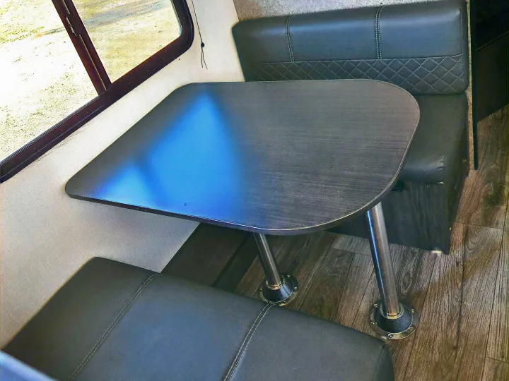 This RV rental features a cozy dinette with a dark table, upholstered benches, and a window for scenic views.. Highland Ridge RV Open Range 2021