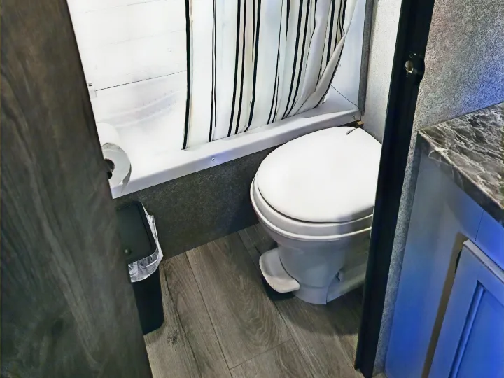 Compact RV rental bathroom showcasing a foot-flush toilet, striped shower, and dark wood-look floor.. Highland Ridge RV Open Range 2021