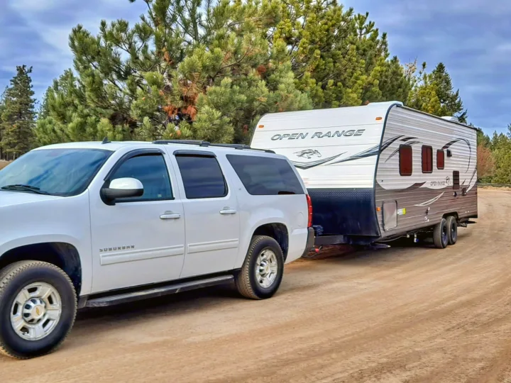 White Suburban SUV towing an Open Range travel trailer on a dirt road, ready for your next RV rental adventure.. Highland Ridge RV Open Range 2021