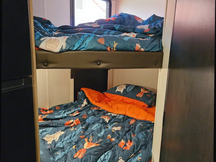 RV rental bunk beds with colorful animal and nature-themed comforters, bright orange sheet, and window view.. Forest River Cherokee Wolf Pup 2026