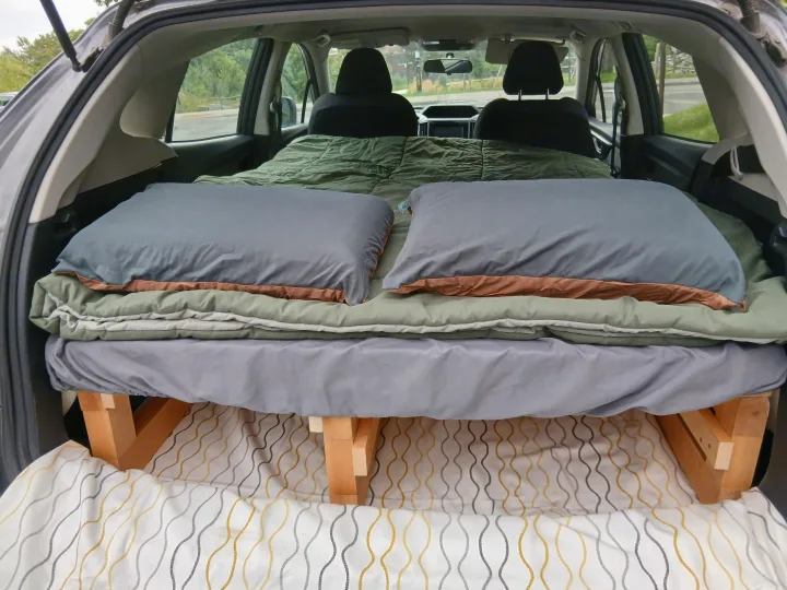 Inside an SUV, a custom wooden sleeping platform with soft bedding creates a cozy bed for car camping, perfect for your next rv rental adventure.. Subaru Impreza 2018