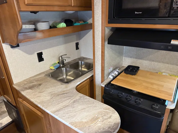 Compact RV rental kitchen with a double sink, microwave, stove, and countertop. Essential amenities for your road trip.. Coachmen Leprechaun 2019