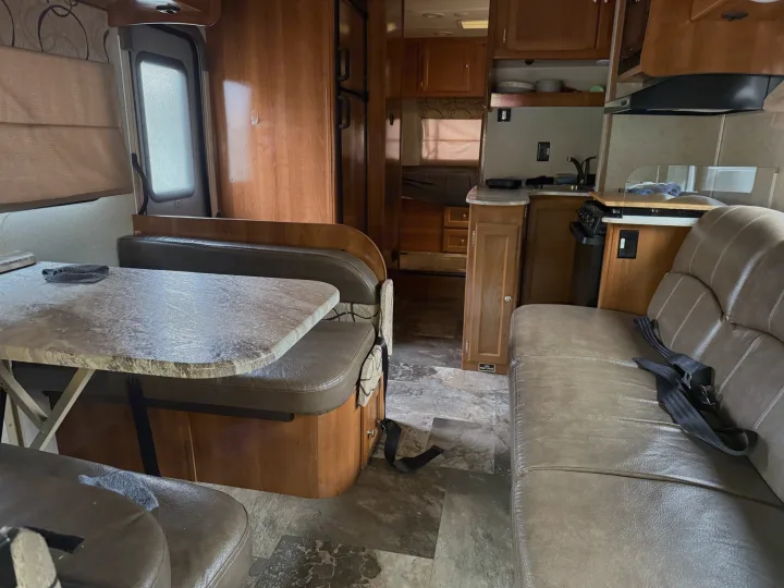 Explore this RV rental's inviting interior: wood-paneled dinette, compact kitchen, and comfy seating. Perfect for adventure travel.. Coachmen Leprechaun 2019
