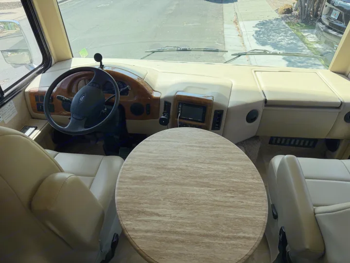 RV rental's spacious interior: driver's cockpit, passenger seat, dashboard, and round dining table.. Thor Windsport 2018