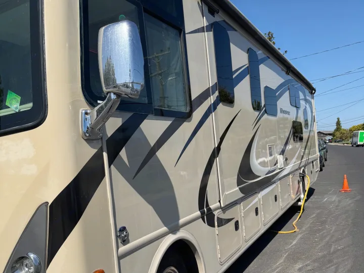 Tan RV rental (Windsport model) parked outside on a sunny day, with a utility hose visible on the street.. Thor Windsport 2018