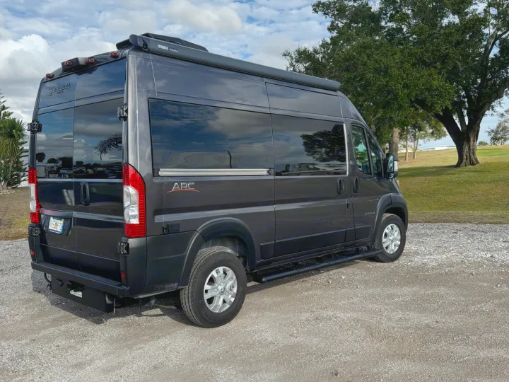 Dark grey Entegra Coach ARC camper van RV rental, fully equipped with a Thule awning, parked on gravel for travel.. Entegra Coach ARC 2025