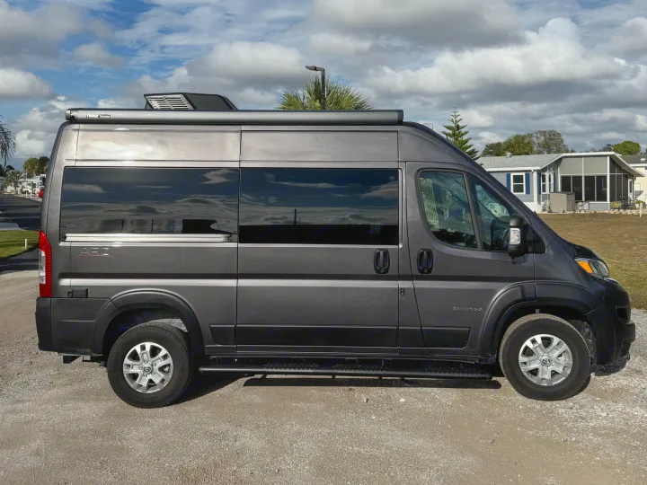 Dark gray Entegra camper van (Class B RV) with a Thule awning, parked on gravel, ideal for rv rental adventures.. Entegra Coach ARC 2025