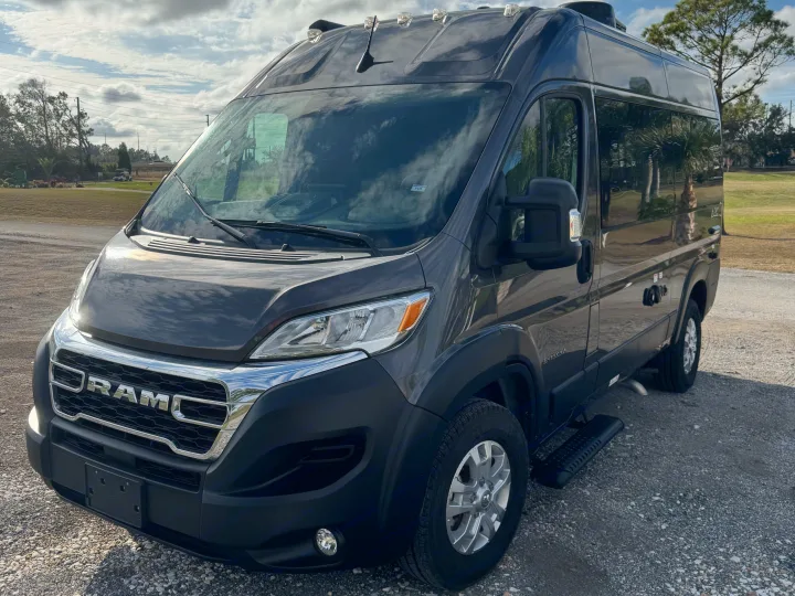 Dark gray RAM ProMaster camper van, an excellent RV rental option, parked outside on a gravel lot under a cloudy sky.. Entegra Coach ARC 2025
