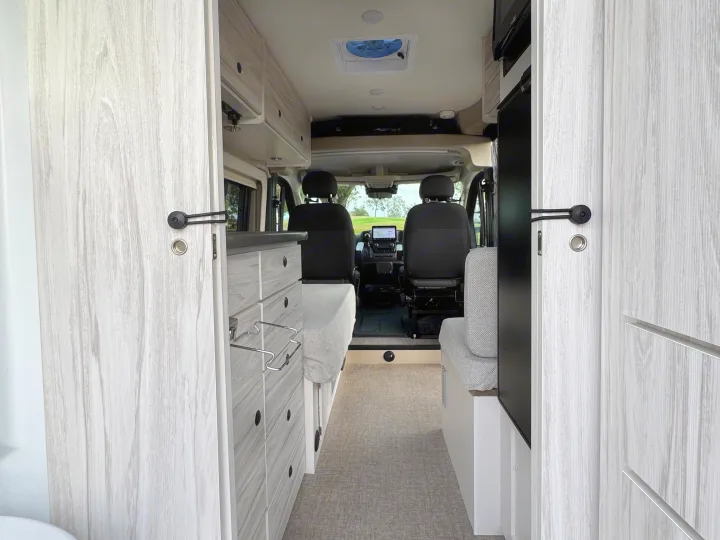 Spacious RV rental interior featuring modern light wood finishes, kitchenette, and comfortable seating leading to the cockpit.. Entegra Coach ARC 2025