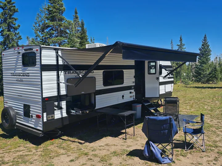 Perfect RV rental for camping: a travel trailer with an outdoor kitchen, awning, chairs, and table under blue skies.. Grand Design Transcend Xplor 2026