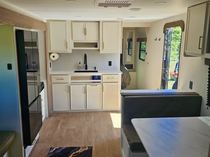 Modern RV rental interior with a bright kitchen, white cabinets, black sink, and a cozy dining booth for travelers.. Grand Design Transcend Xplor 2026