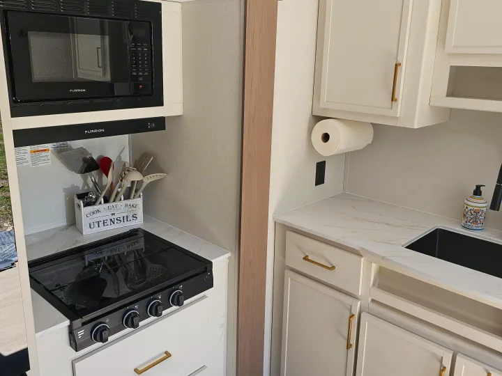 Modern RV rental kitchen showcasing a Furrion microwave, two-burner stove, sink, and sleek white cabinets.. Grand Design Transcend Xplor 2026