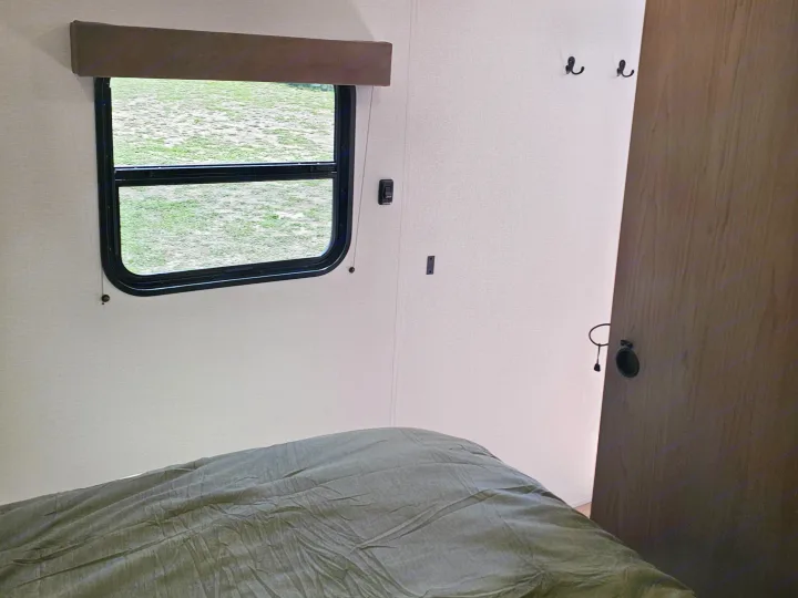 Cozy rv rental bedroom interior featuring a window with a green view, a comfortable bed, and wall hooks.. Grand Design Transcend Xplor 2026